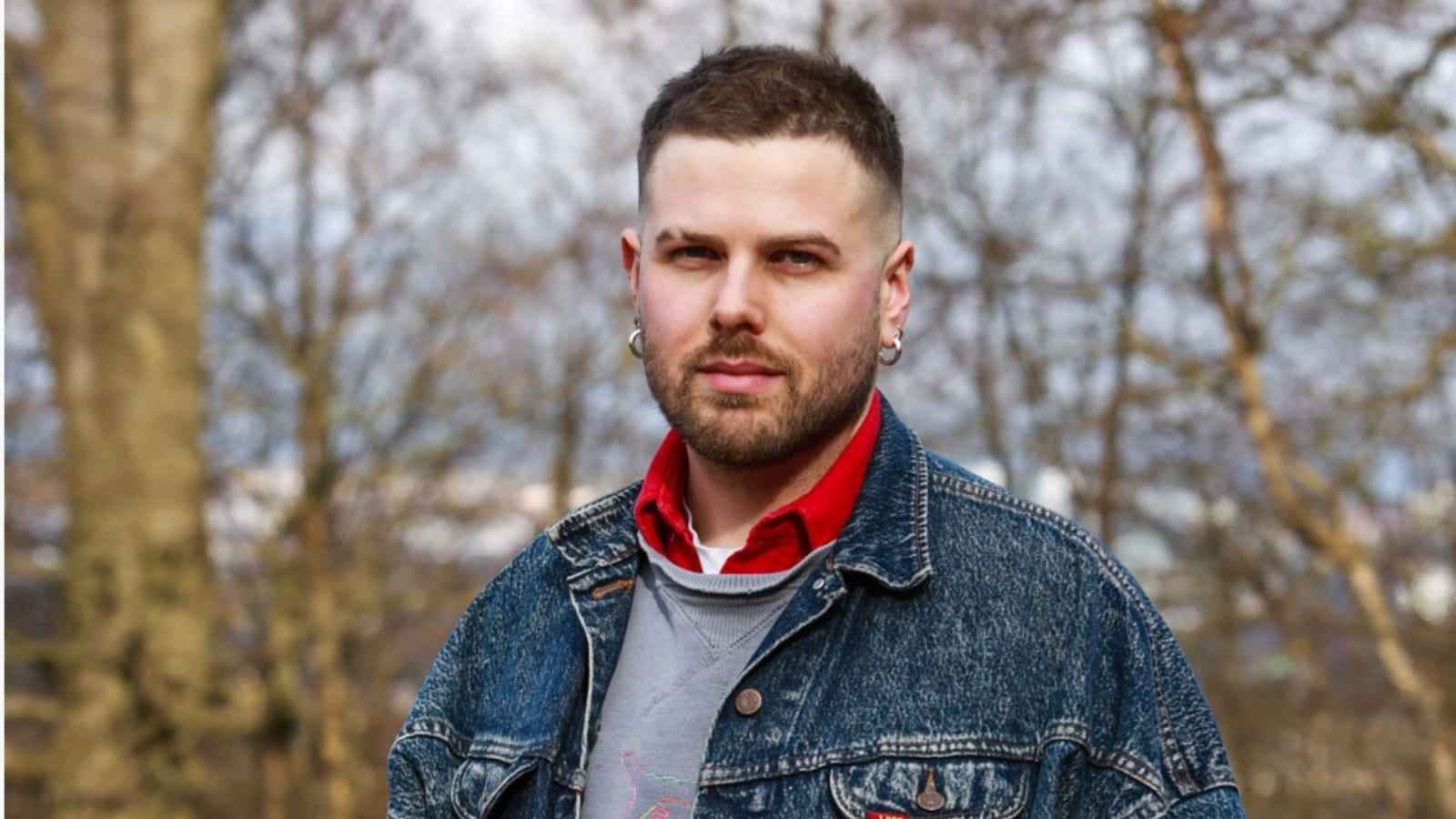 Andrew Black stands in front of a woodland area, looking at the camera