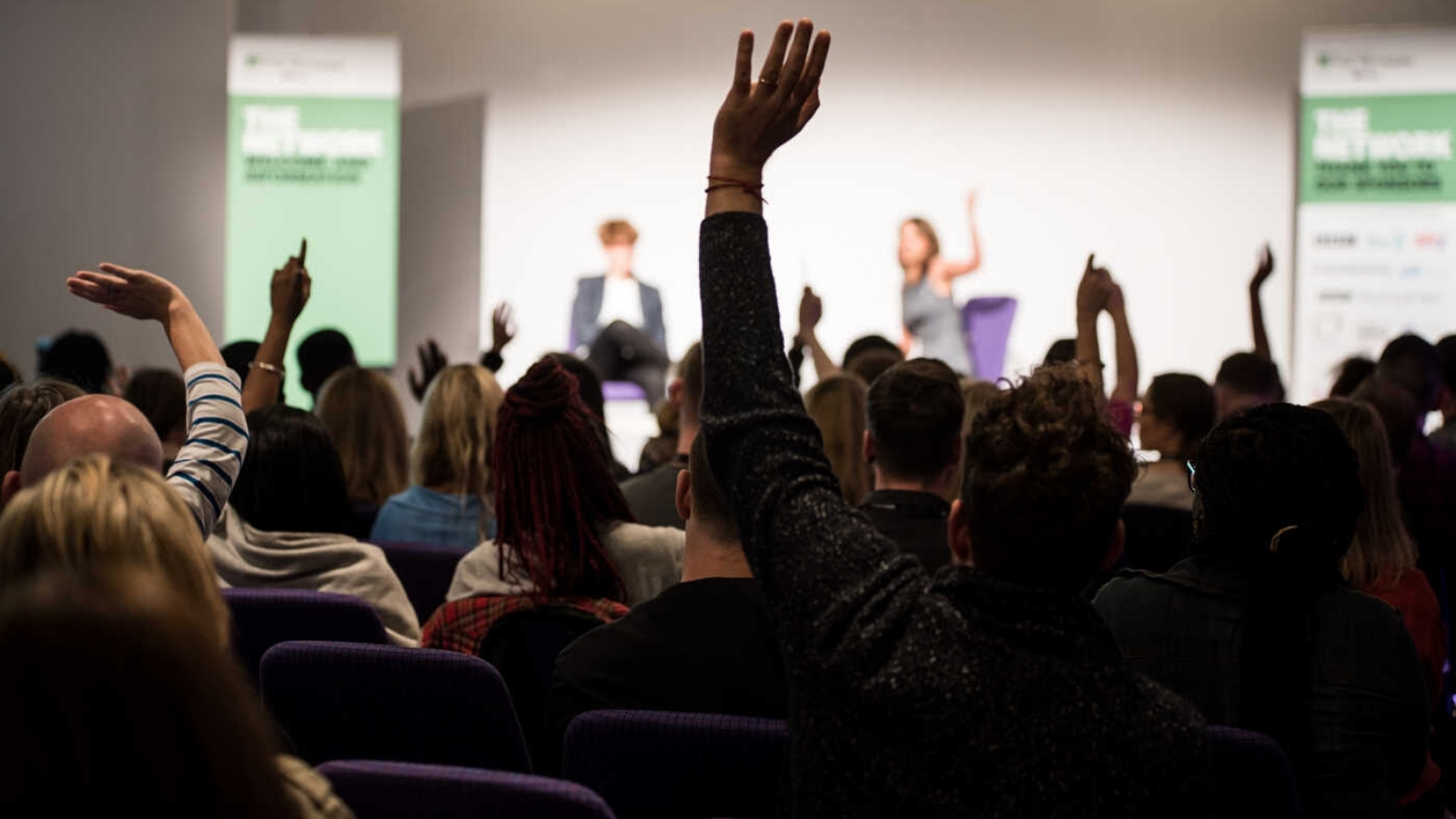 An audience sit watching people on stage at the Edinburgh TV Festival, several people have their hands raised for questions