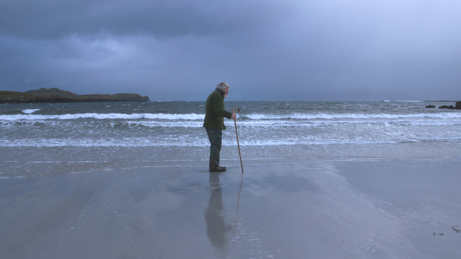 A man walking along a beach with a moody grey sky in the distance