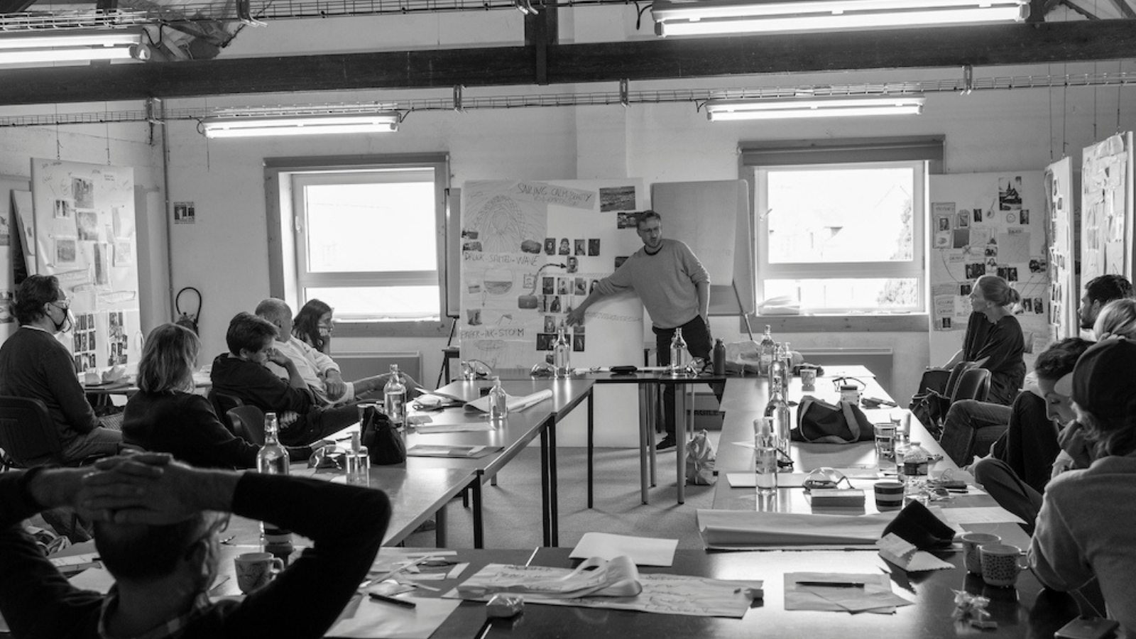 People chatting in a room around a large table with papers spread across it. Taken at a Less is More residency.