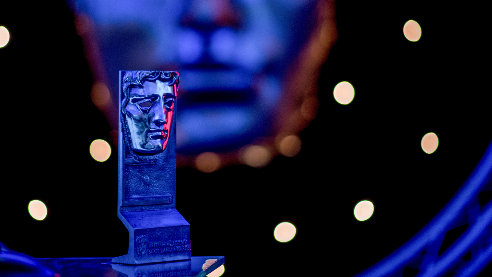 Bafta award sitting on a table and lit up with blue and red lights.