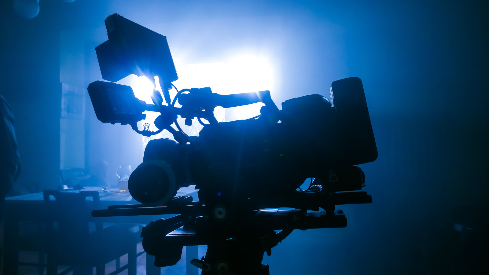 A film camera in silhouette, with soft blue and white light filtering through from behind it