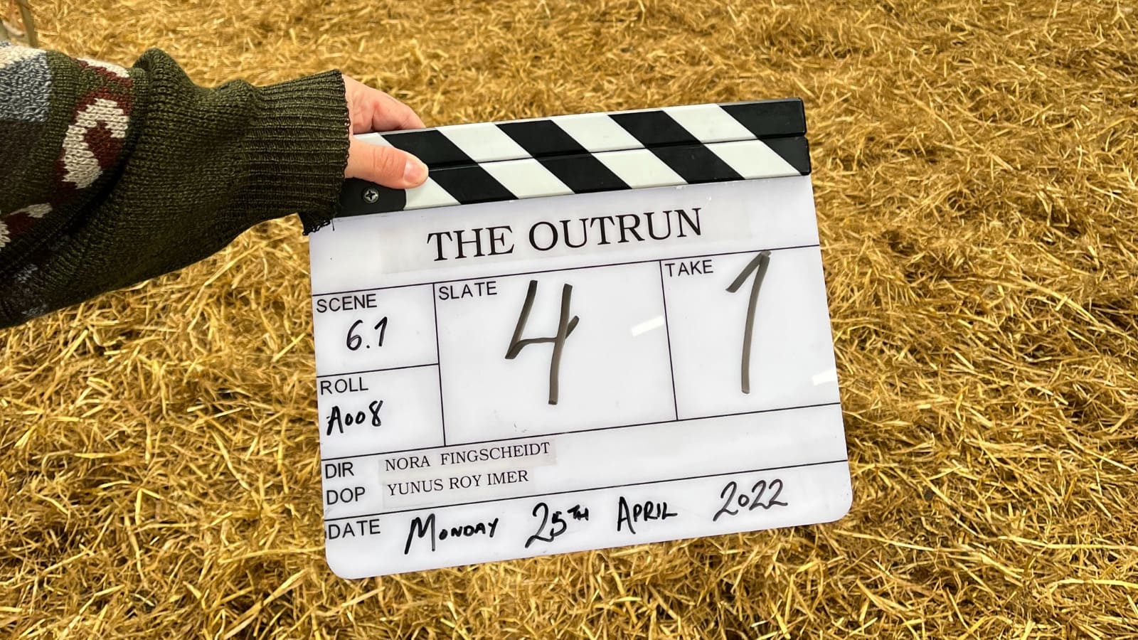 A hand holding a clapperboard outdoors which reads the Outrun and slate 4