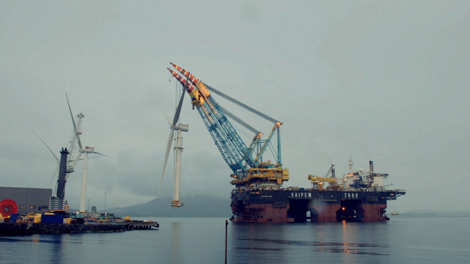 An oil rig during an overcast wet-looking day. Still from The Oil Machine.