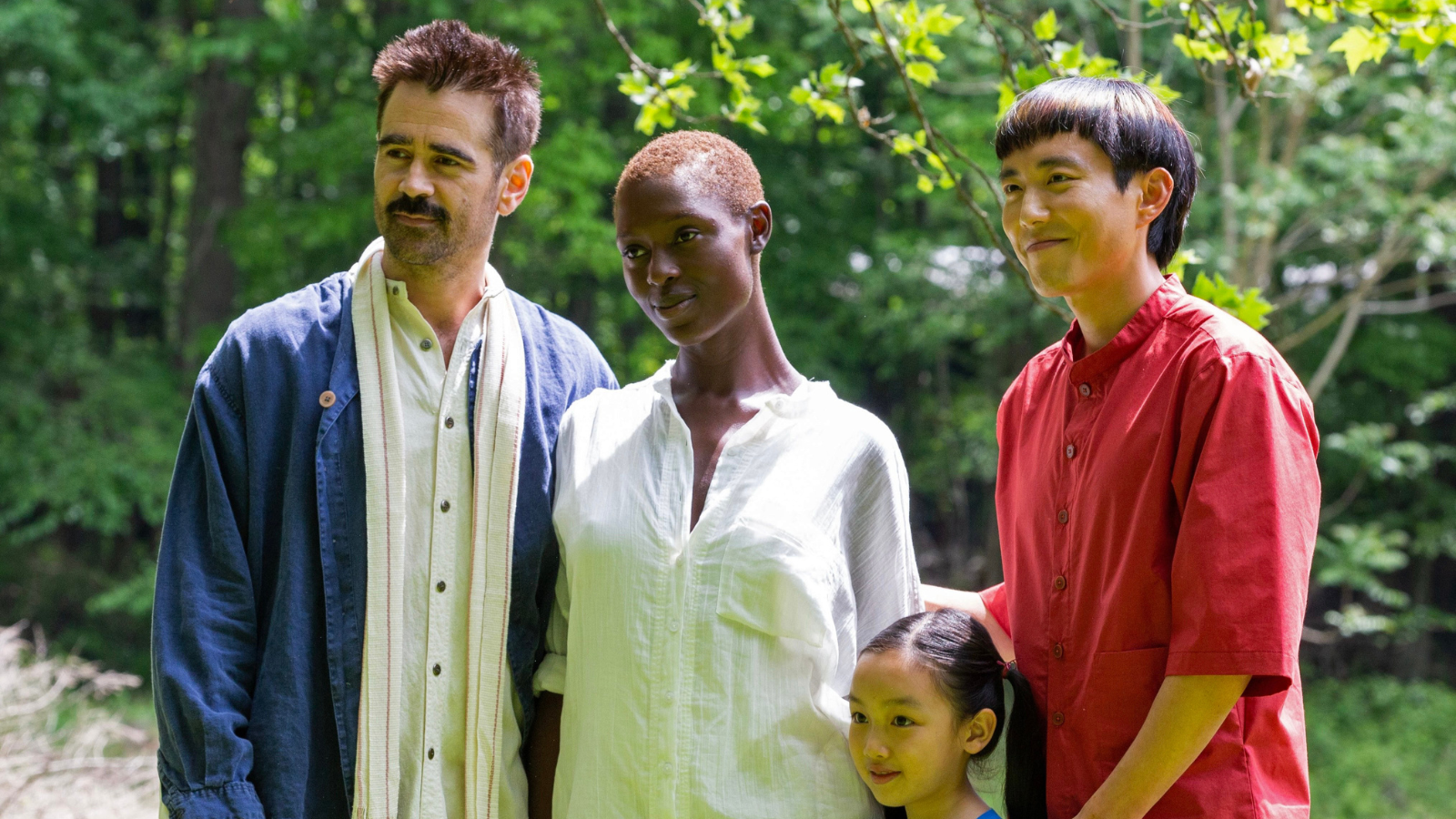 Still from After Yang. Four people standing together on a bright day, with leafy bushes and trees around them: a man (Colin Farrell), a woman (Jodie Turner-Smith), a young girl (Malea Emma Tjandrawidjaja) and another man (Justin H.Min).