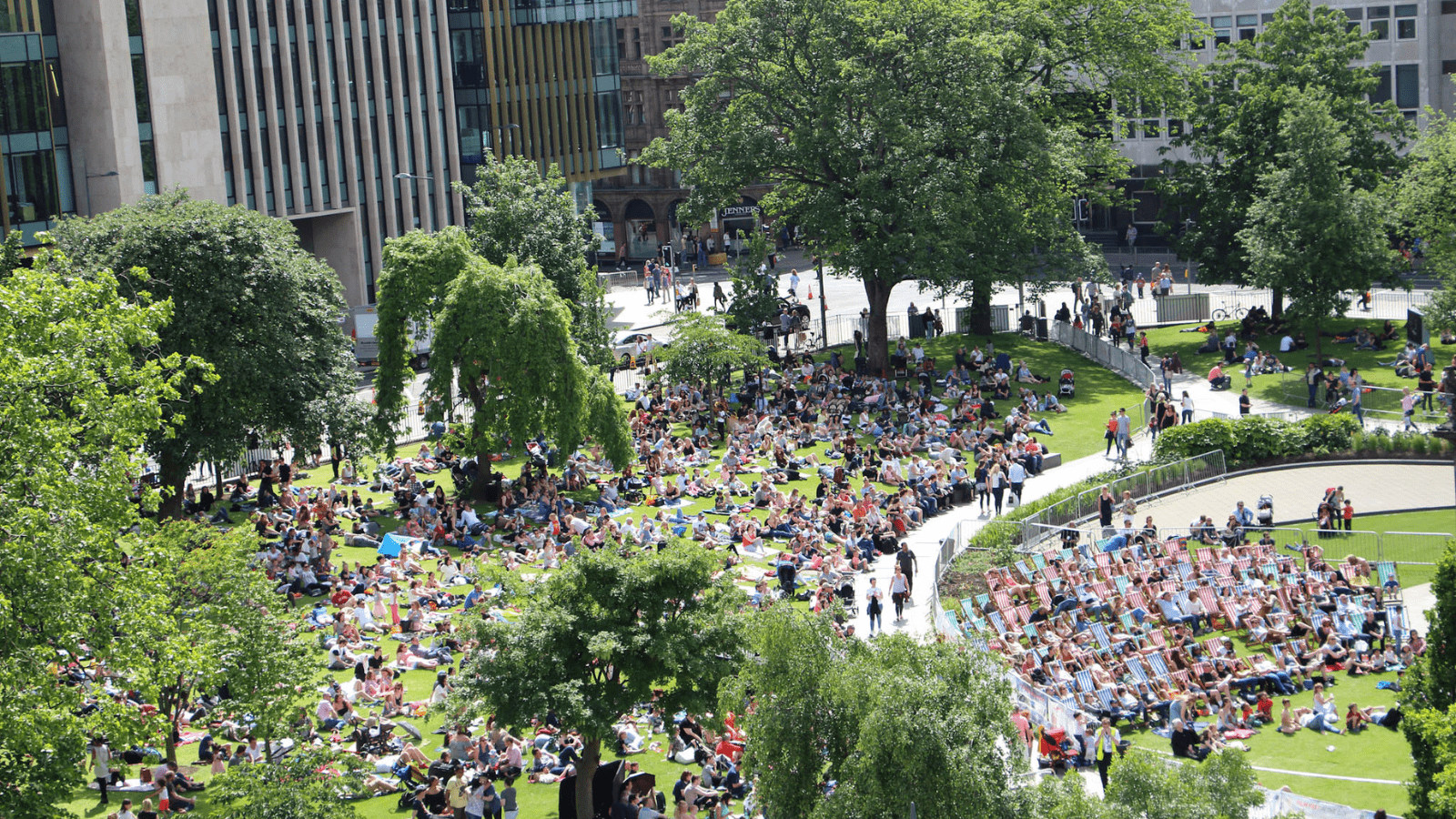 People lounging on striped beach style chairs in a leafy park (St Andrew Square) during a summer's day.