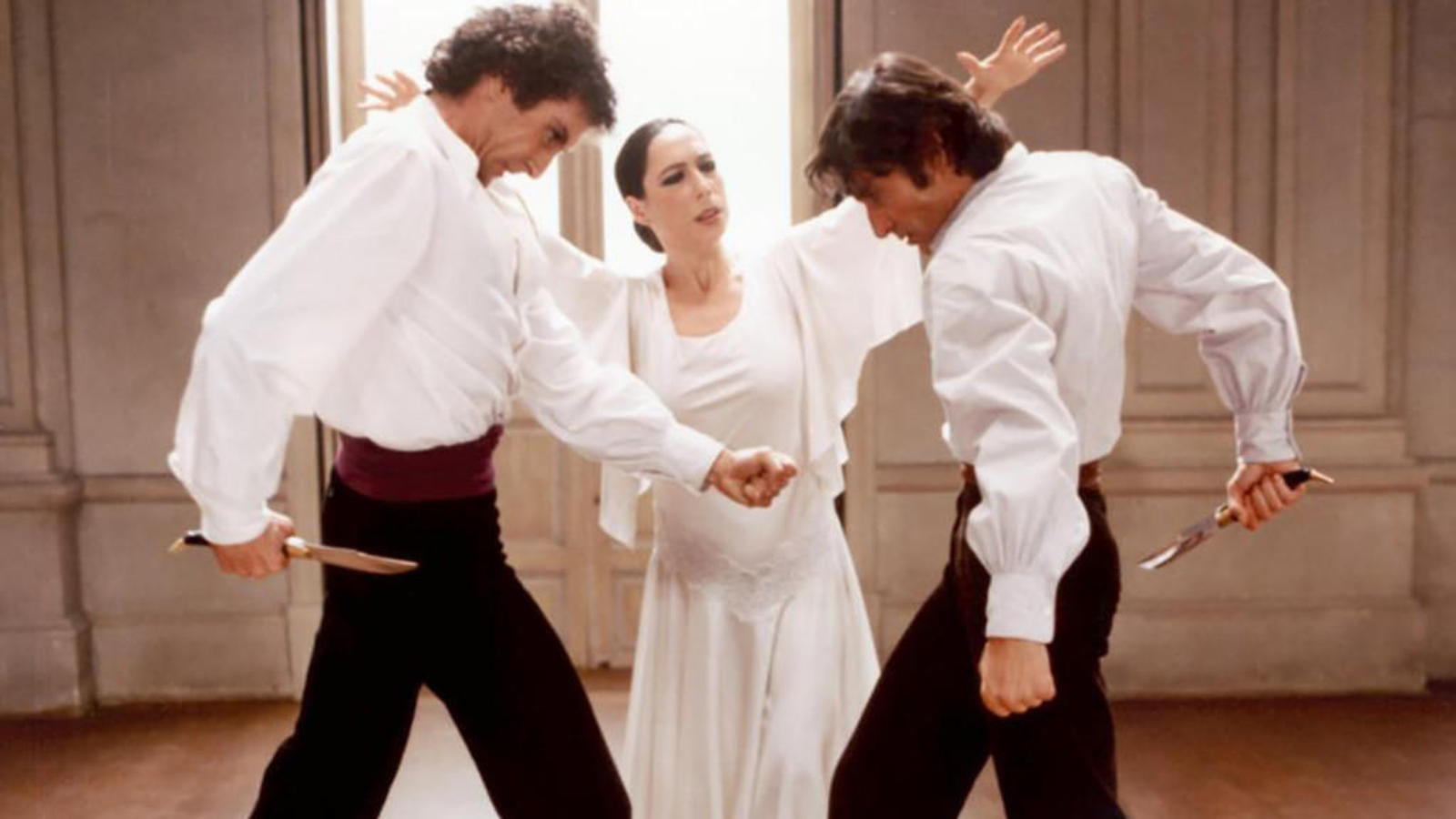 Still from Bodas de Sangra. A WOMAN AND TWO MEN DRESSED IN BACL AND WHITE STANDING OPPOSITE EACH OTHER WHILE DANCING.