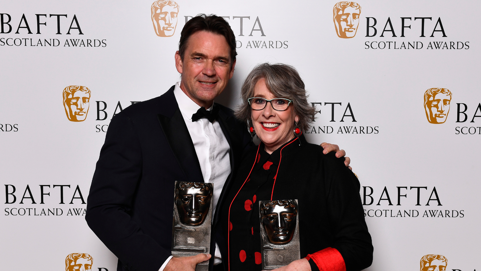 Dougray Scott and Phyllis Logan holding BAFTA Scotland trophies.