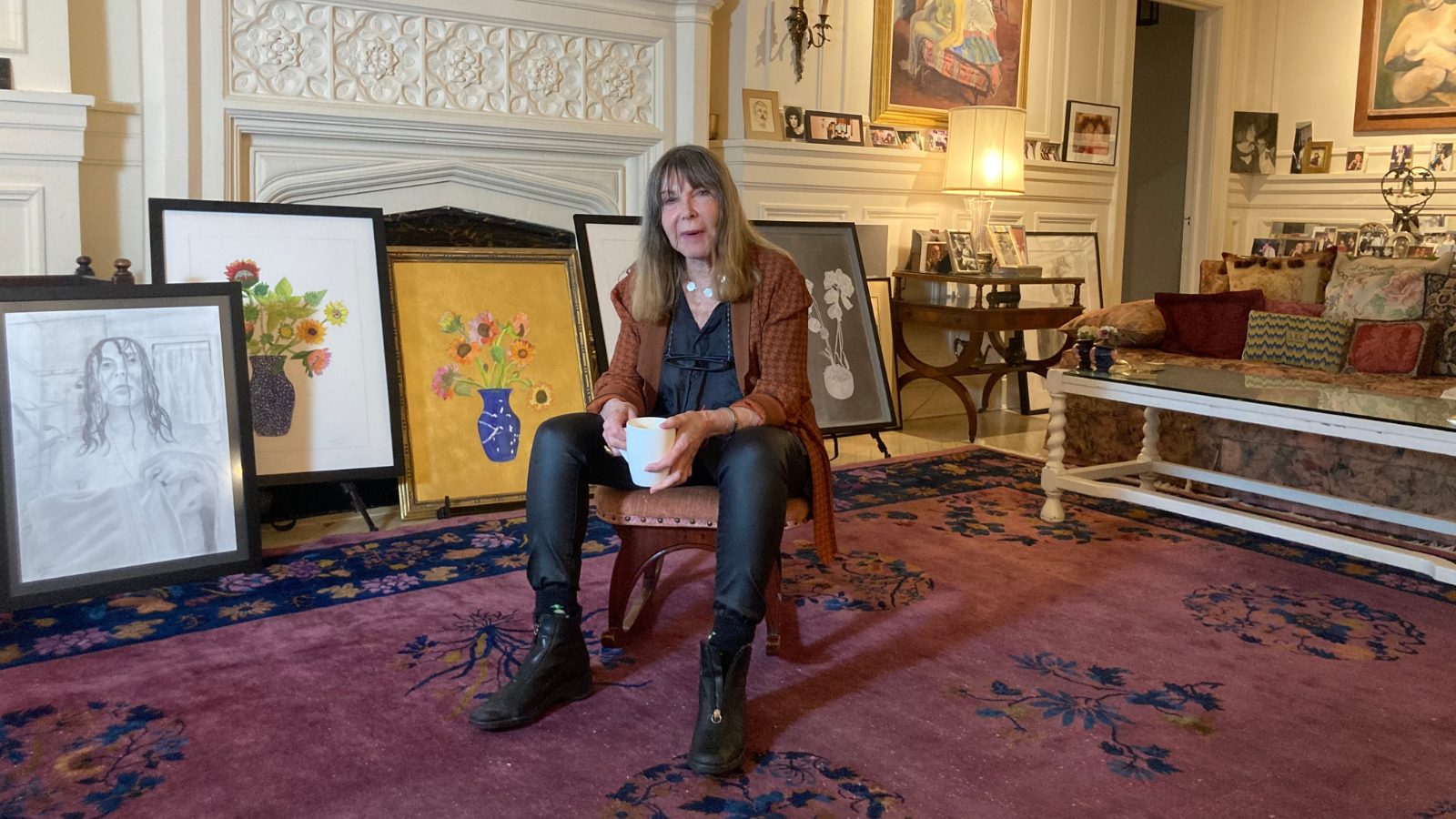 Lee Grant sitting on a stool in large room with pictures hanging on the wall.