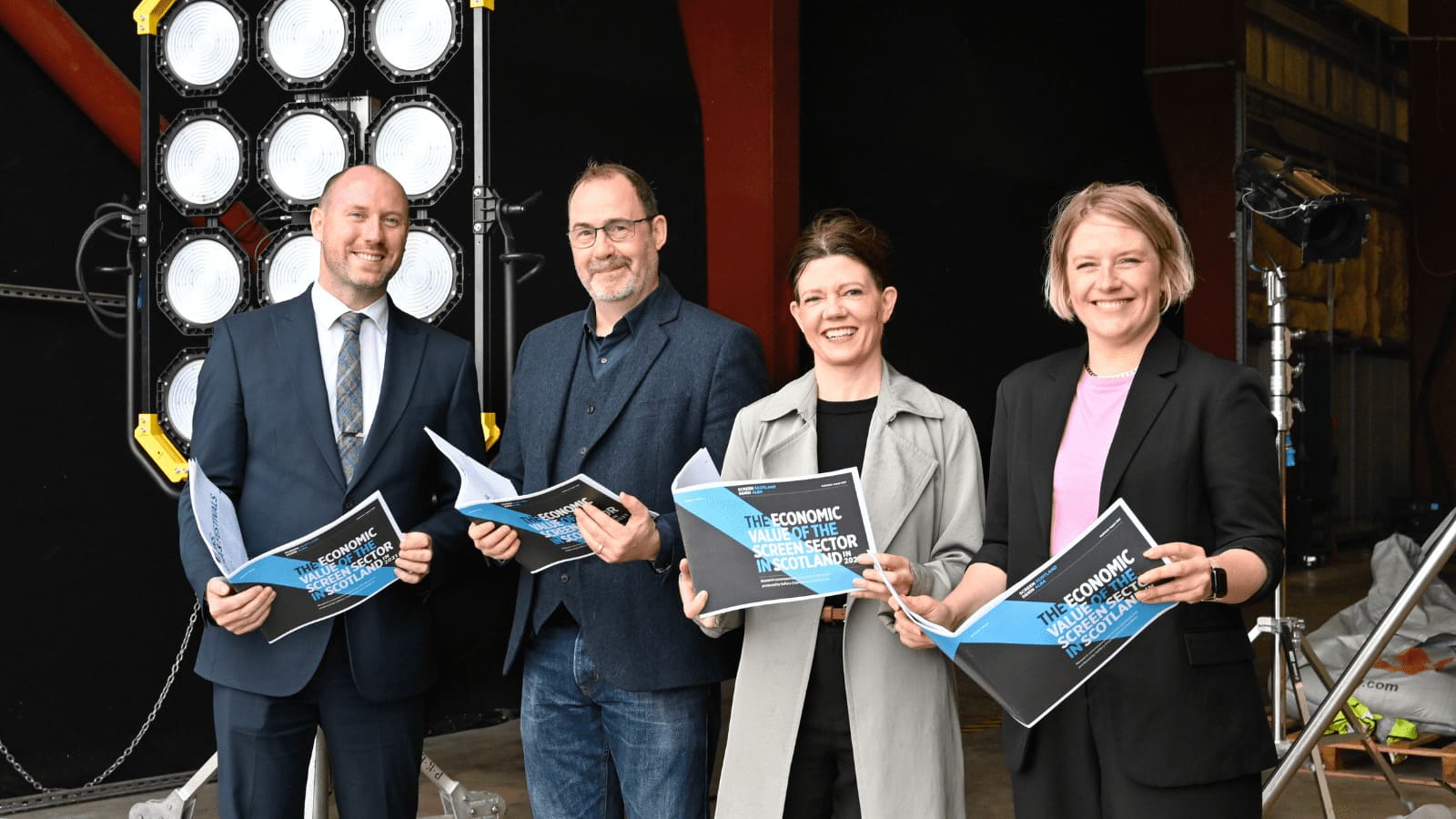 Isabel Davis (Exexcutive Director of Screen Scotland), Wellbeing Economy Secretary Neil Gray, Daisy Mount (Prime Video's Development Executive), and David Smith (Director of Screen Scotland) standing holding the economic impact report