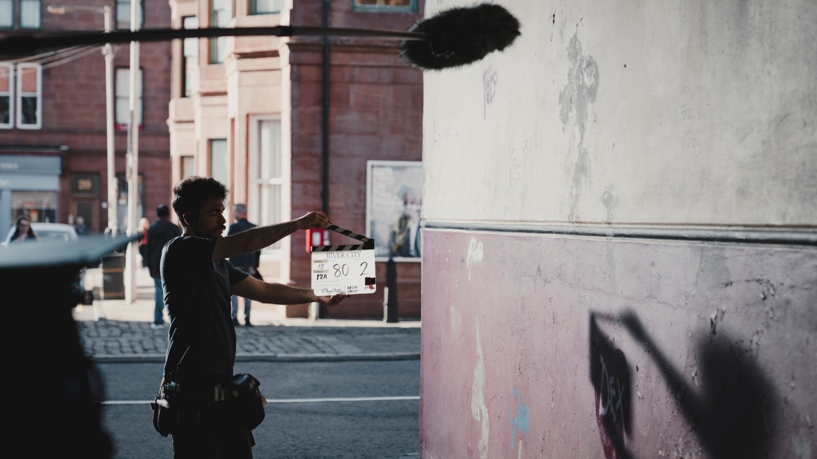 A man holds a clapper board reading River City on it on a city street