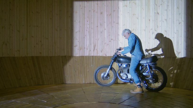 Man stand next to a motor cycle lit up by stage lights