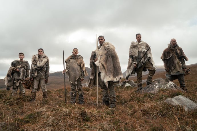 Six stone-age people stand on a field in the Scottish highlands