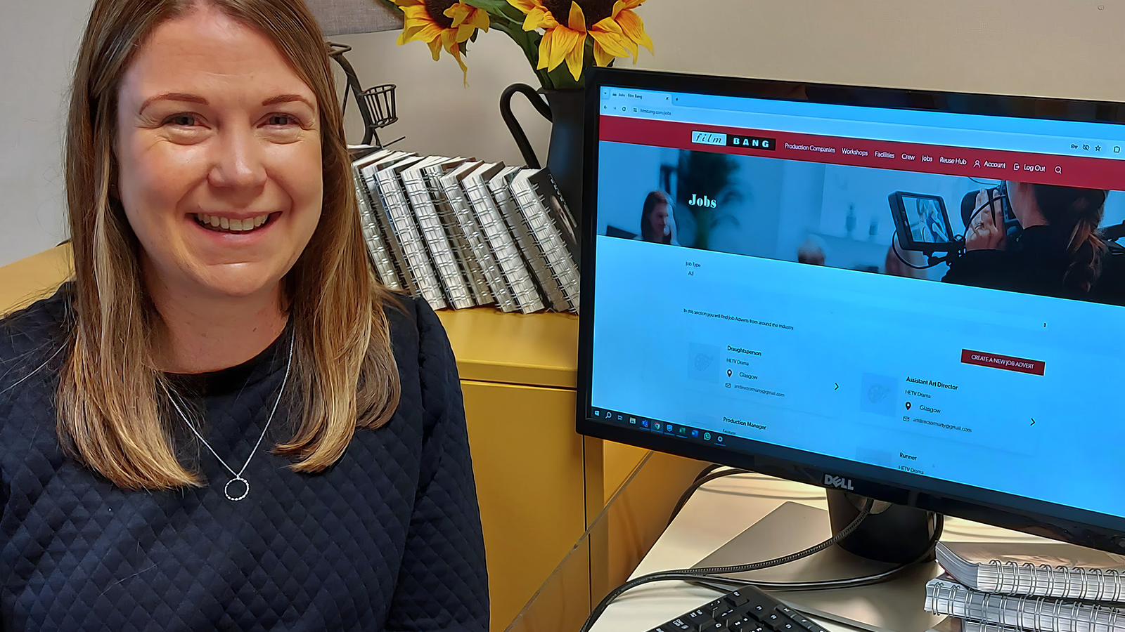 A woman sits next to a computer screen which shows a Film Bang webpage about job listings in screen in Scotland