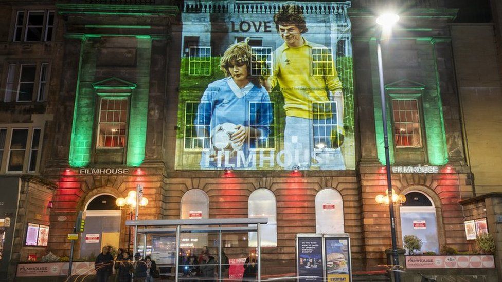 The outside of the Filmhouse cinema in Edinburgh with a still from the film Gregory's Girl is projected on it, featuring a man and a woman in football kits.