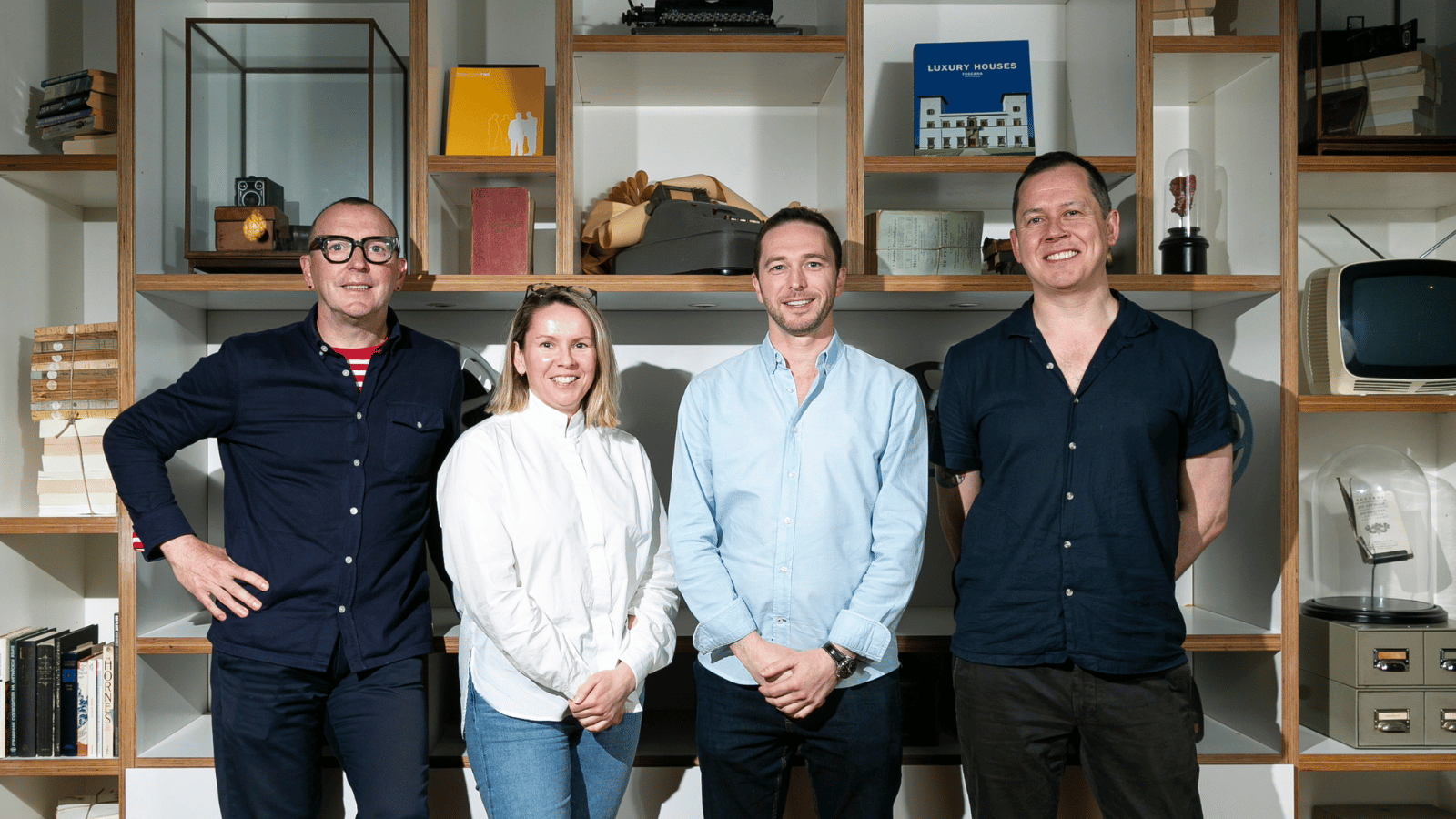 Paul Murray, Amy Jackson, Ken Petrie and Reece Cargan stand in front of a set of shelves, covered with objects including books and a typewriter