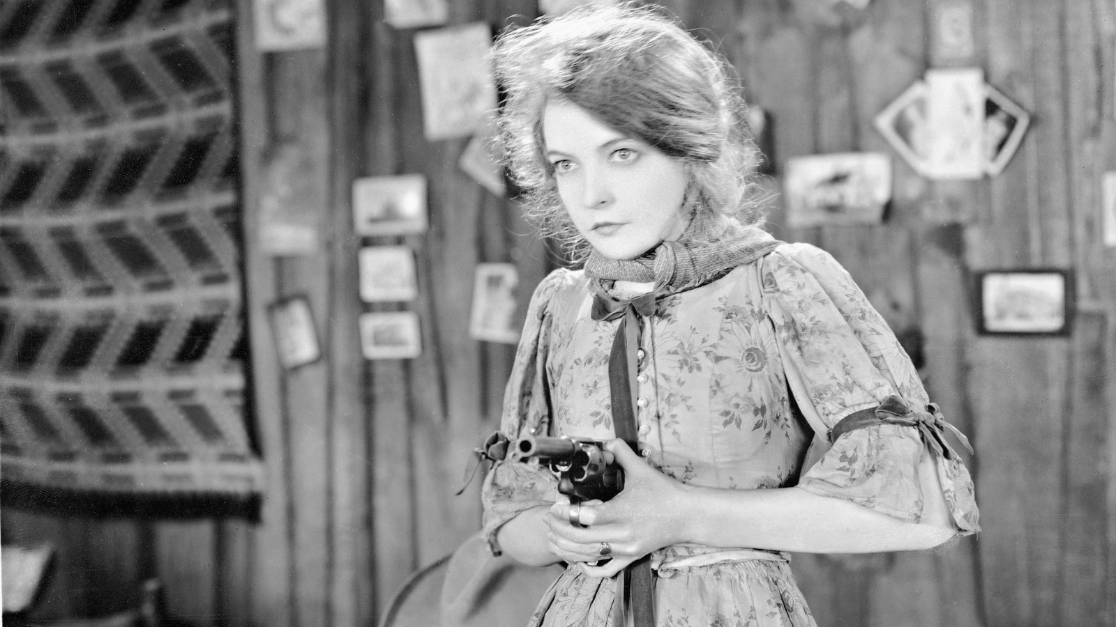 this black and white still from the film The Wind features actress Lillian Gish looks off screen to the left of the image while pointing a gun that she holds in her hands
