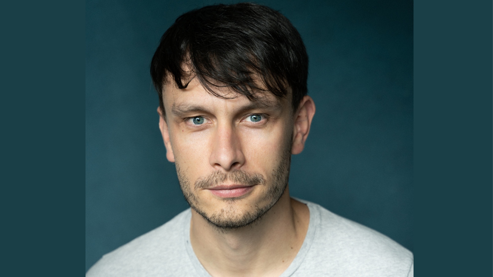 Headshot of actor Richard Gadd, who wears a white t-shirt and is standing against a dark green background.