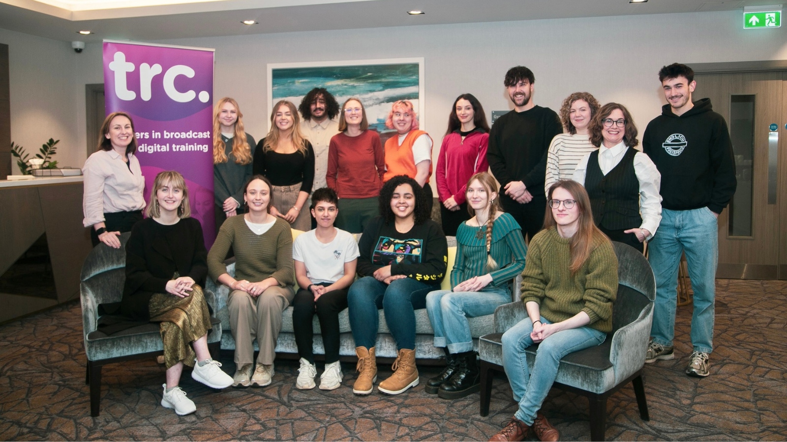 Reset 2 trainees with TRC's MD Claire Scally and Deputy MD Beverley McMillan, sitting in two rows in a room with a TRC pop up banner in the background