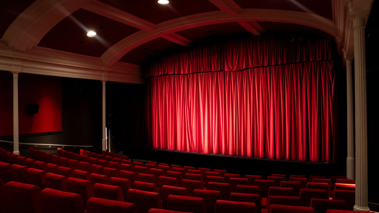 A red curtain is drawn across a cinema screen, with rows of red seats facing forward