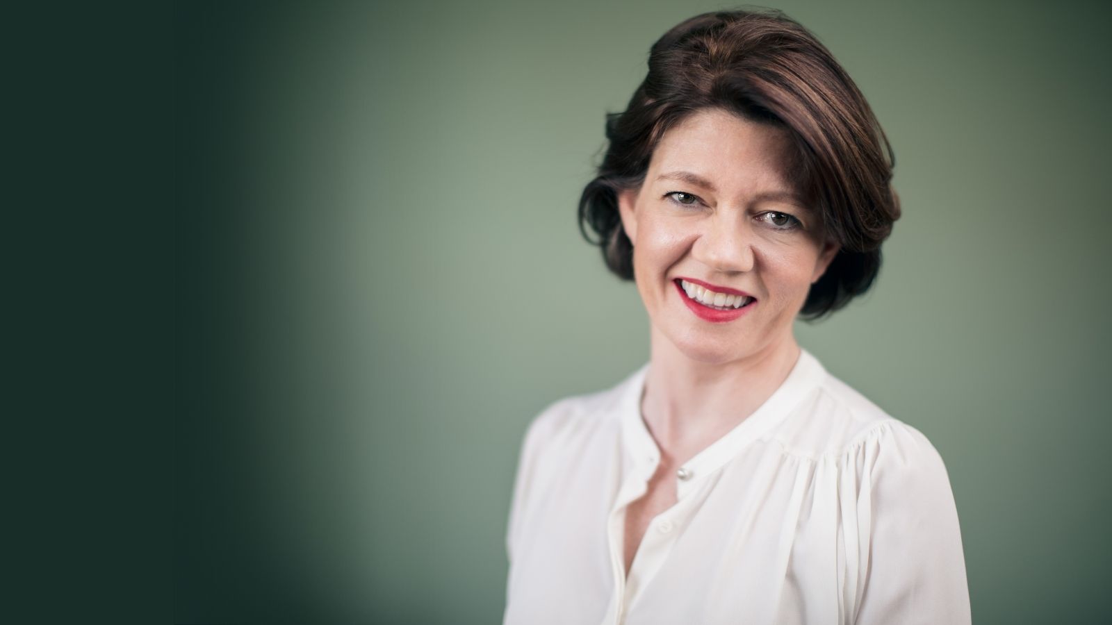 Isabel Davis sits in front of a green background, wearing a white shirt