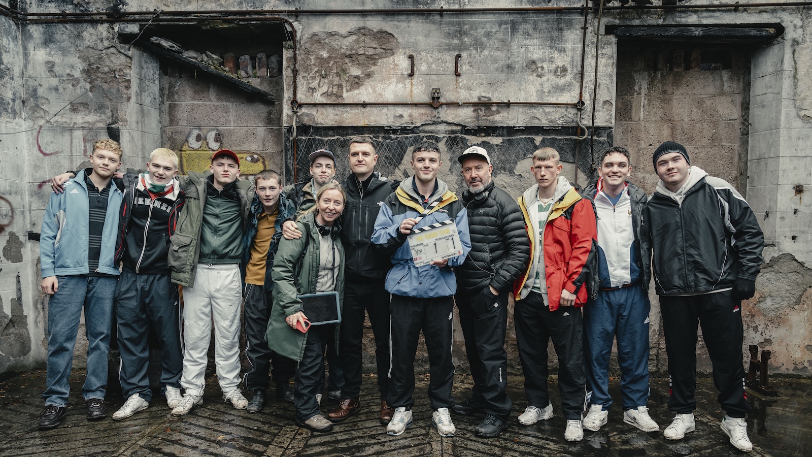 The cast and director and producer of The Young Team stand in a row - the cast are all wearing various styles of tracksuit