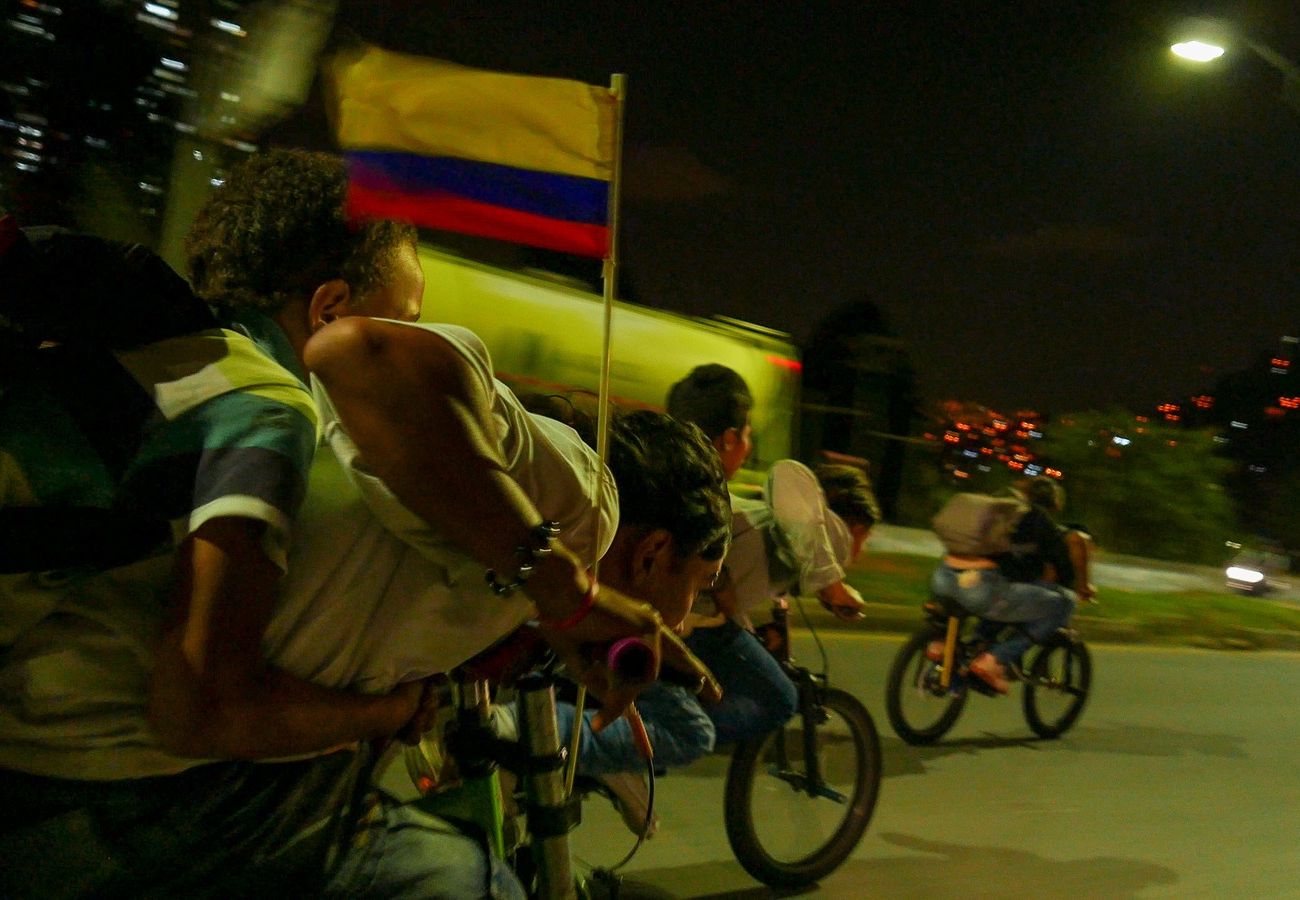 A still image from the cycling documentary ‘Cyclovia’, showing a group of young people cycling down a dimly lit street with a Colombia flag attached to one of the bikes. Image credit: Sonja Henrici Creates / Parcel of Rogues, Casatarantula, Real Lava, Story AB.