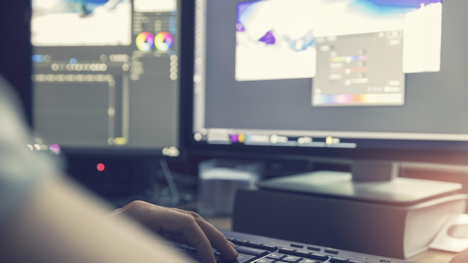 A person just out of shot works on colour grading on an editing suite across two computer screens