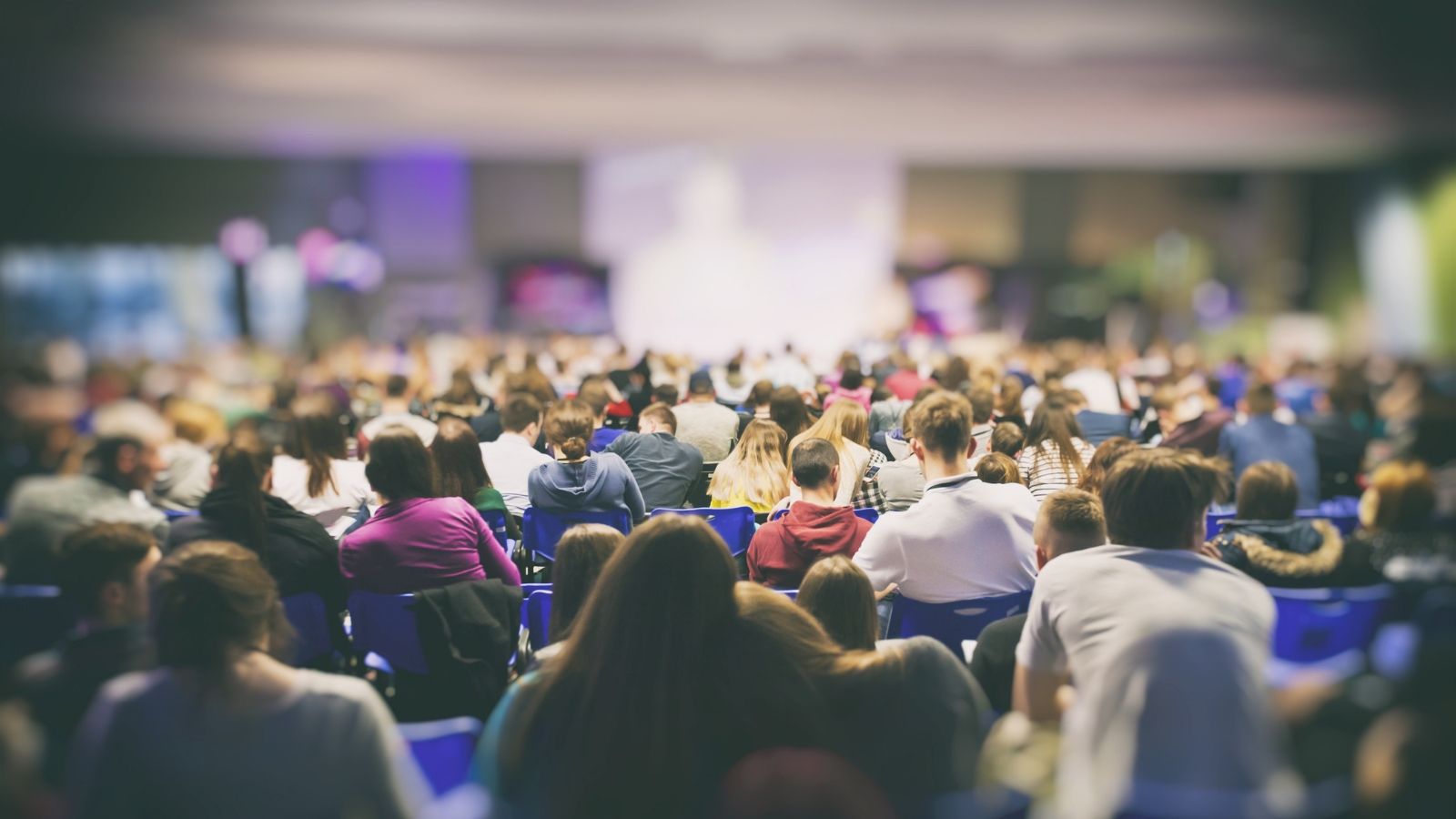 An audience sit at a conference, the image is blurred out