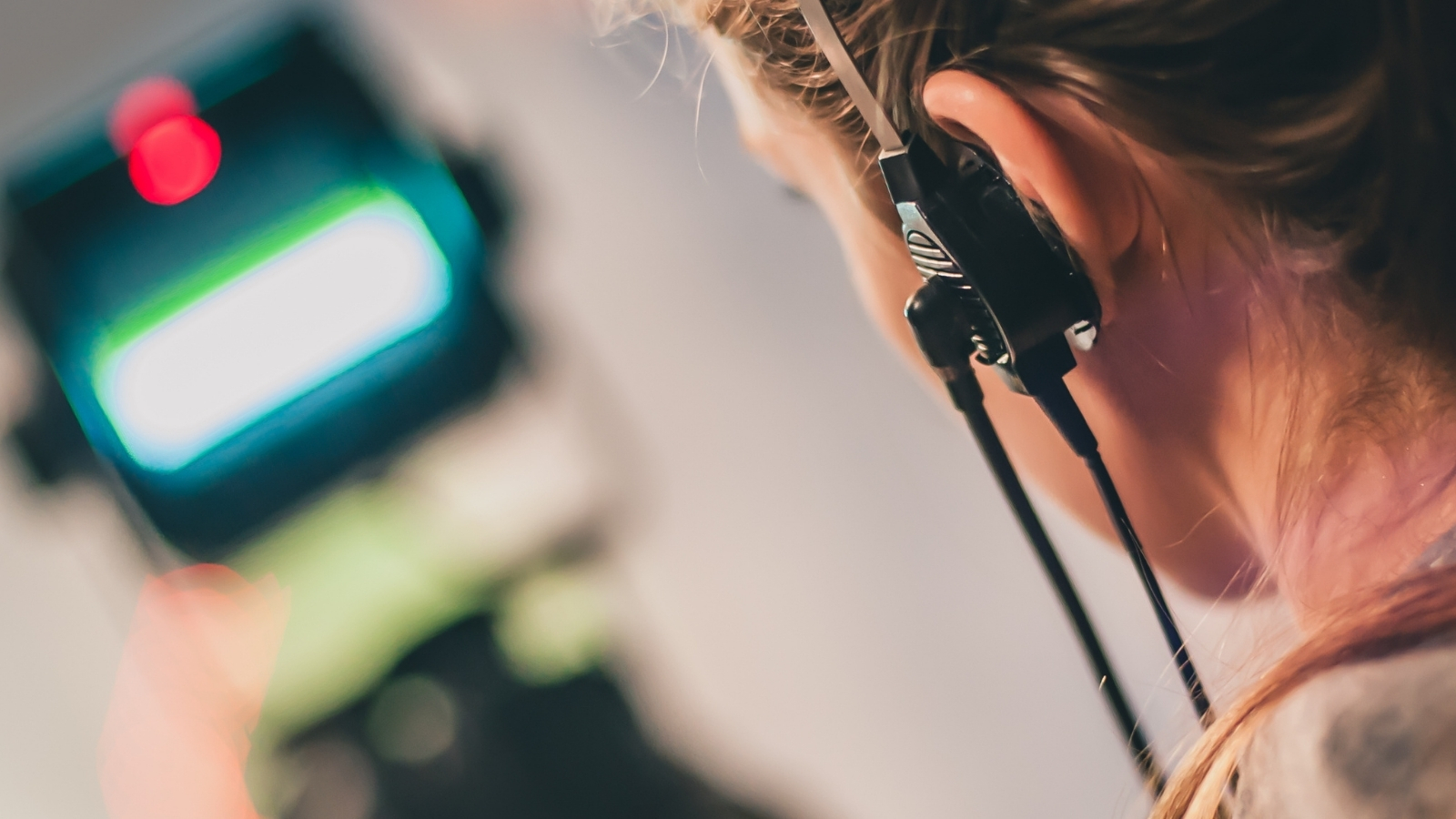 A close up image of a member of crew working on set of a production, wearing an earpiece and looking into a monitor