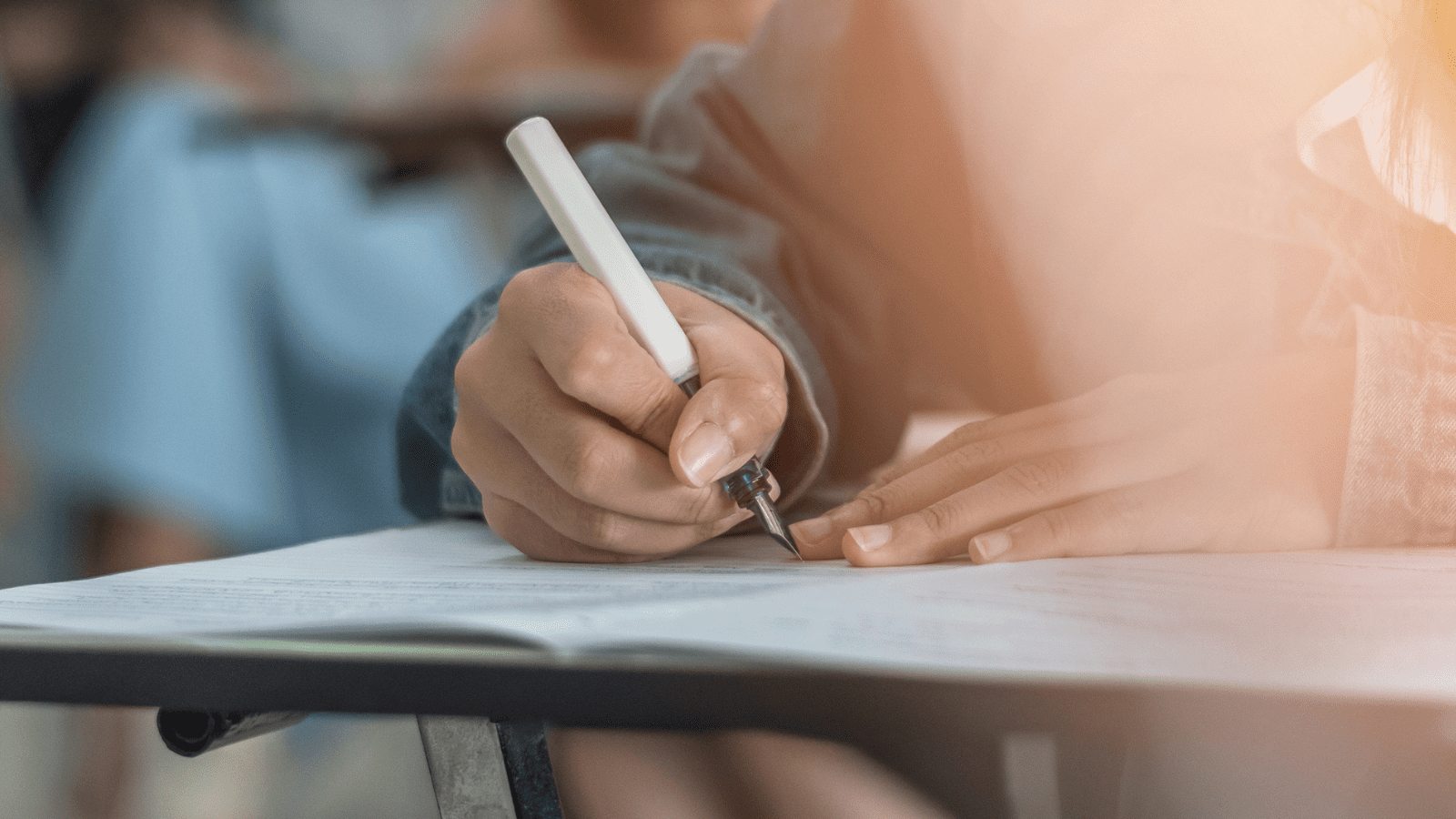 A person sits at a desk writing in a jotter