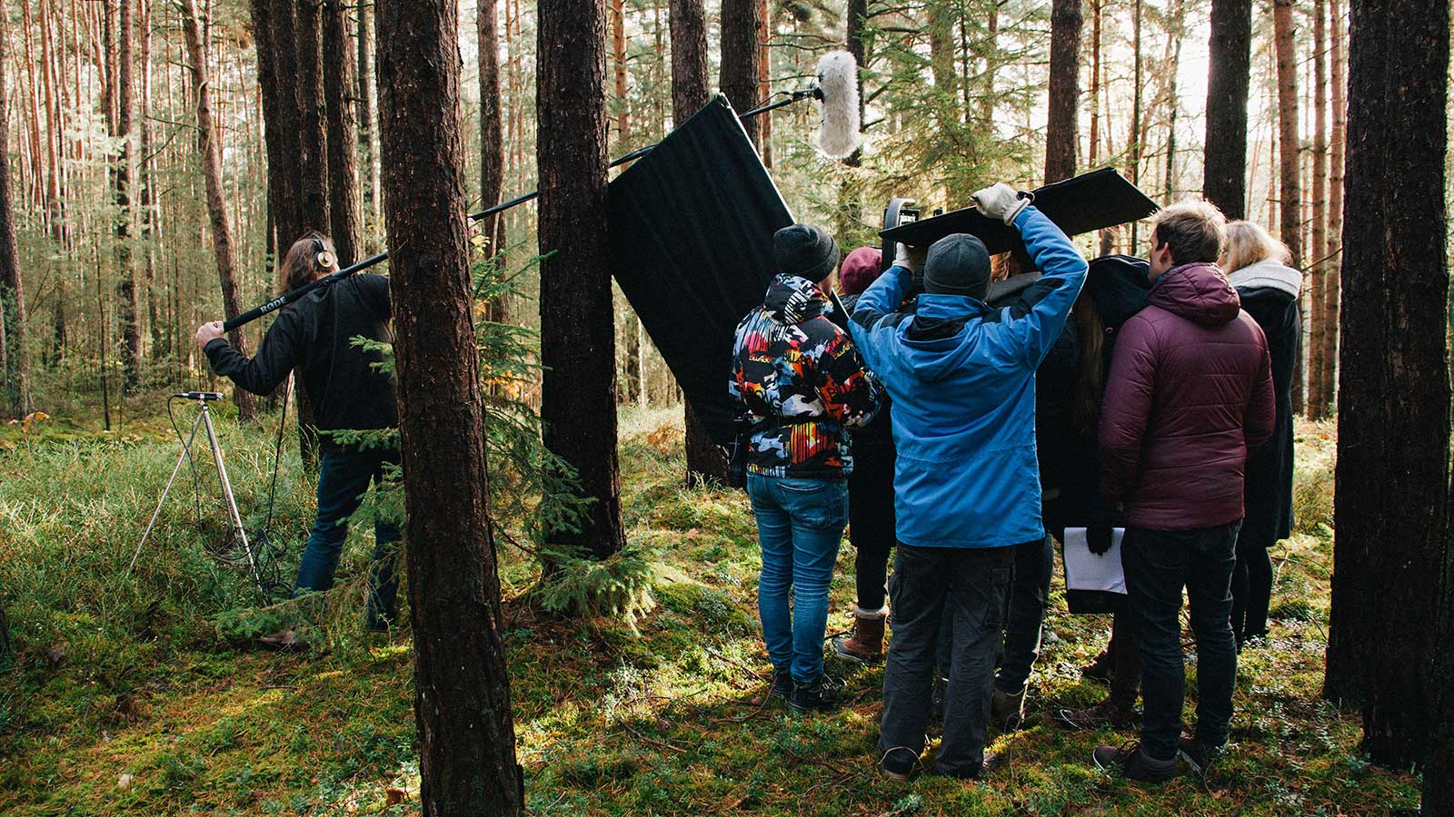 A group of crew are filming outdoors in the woods