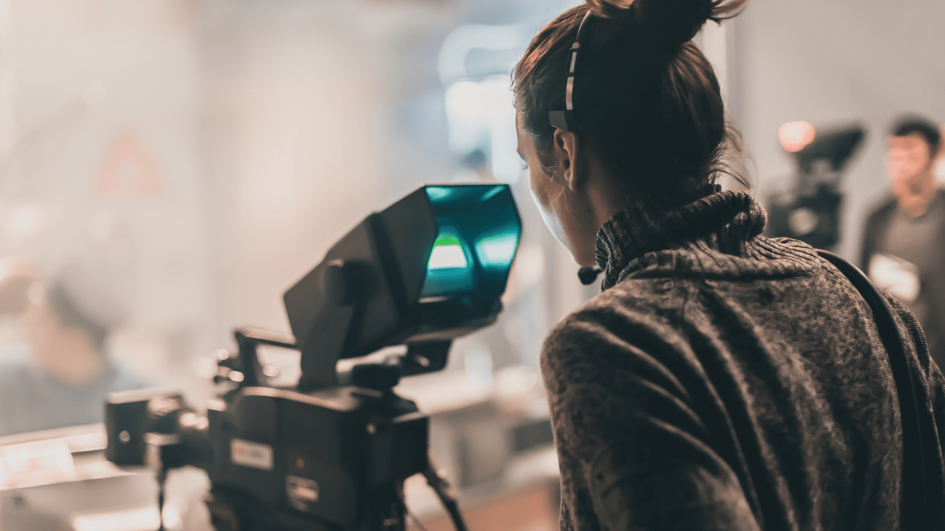 A person wearing a grey jumper and a headset standing behind a studio camera