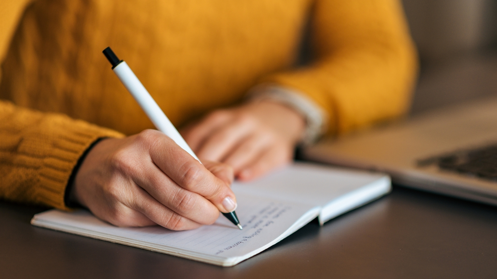 A person sits at a desk writing in an open notebook