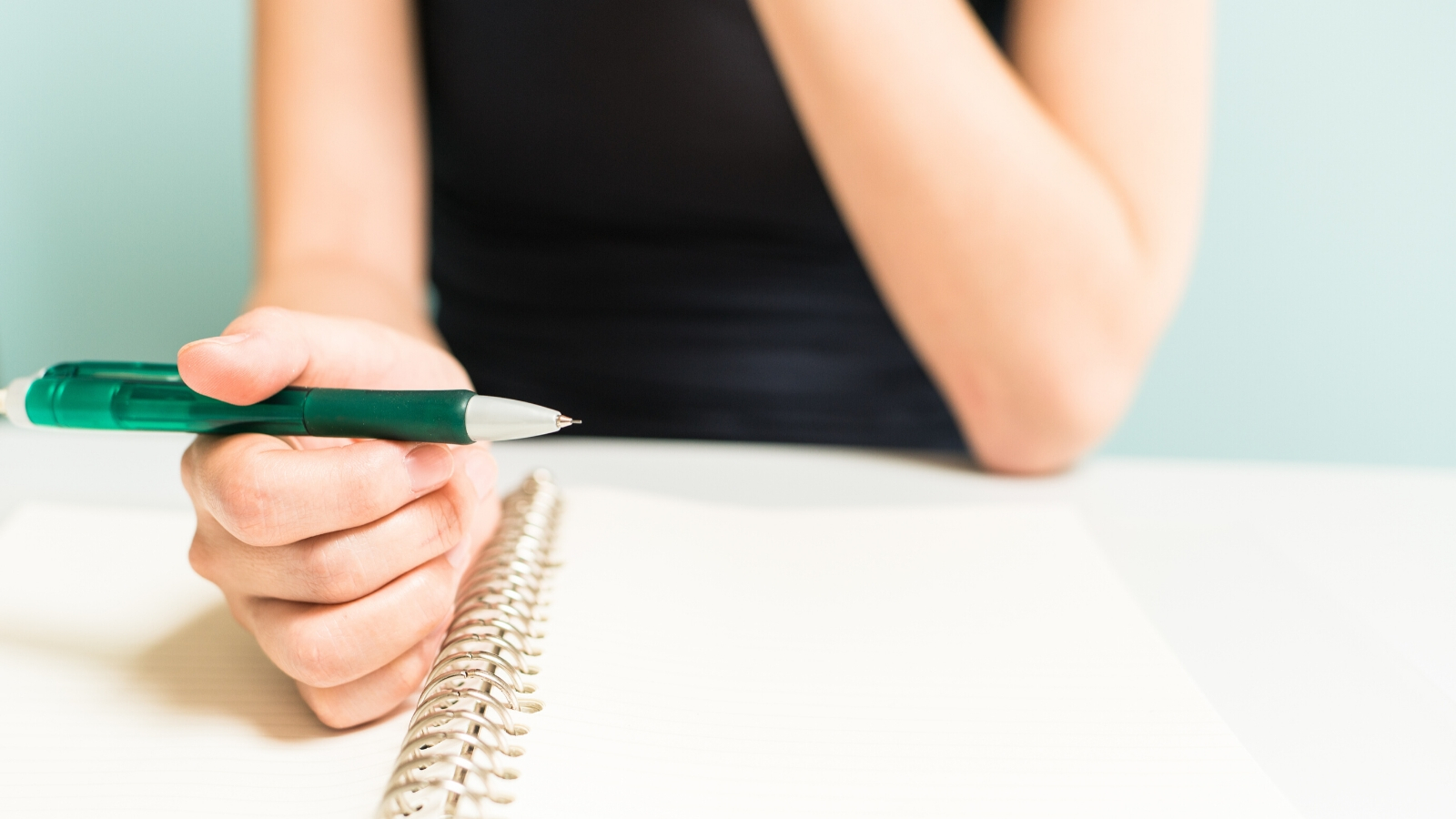 A person sits at a table holding a pen in front of some paper